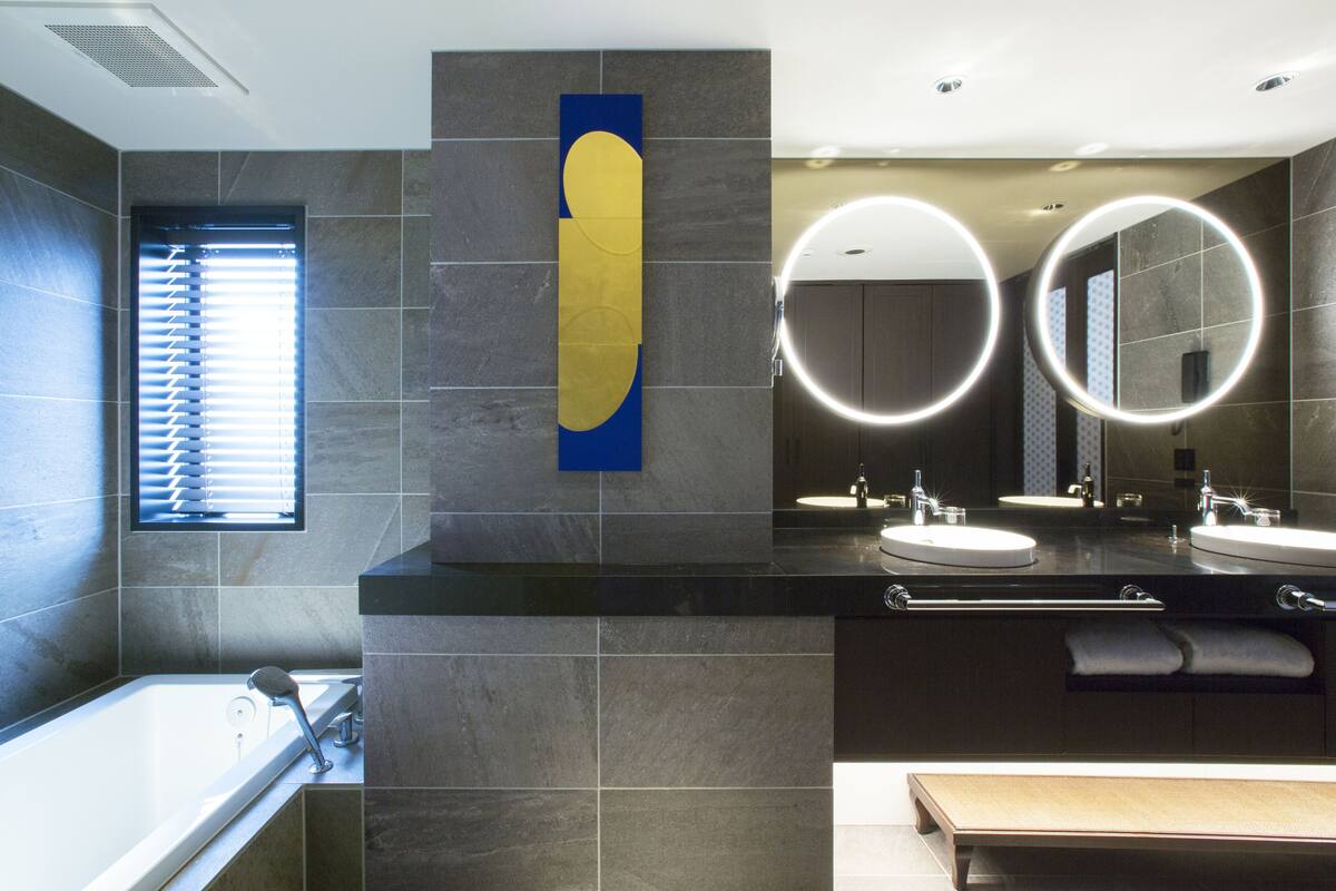 Une salle de bain moderne dotée d’une grande baignoire, de deux lavabos et d’un miroir avec des lumières disposées en cercle.
