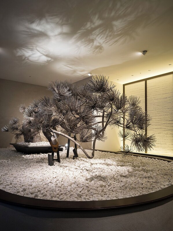 Una habitación con suelo de piedra circular, un bonsái y un biombio japonés tradicional.