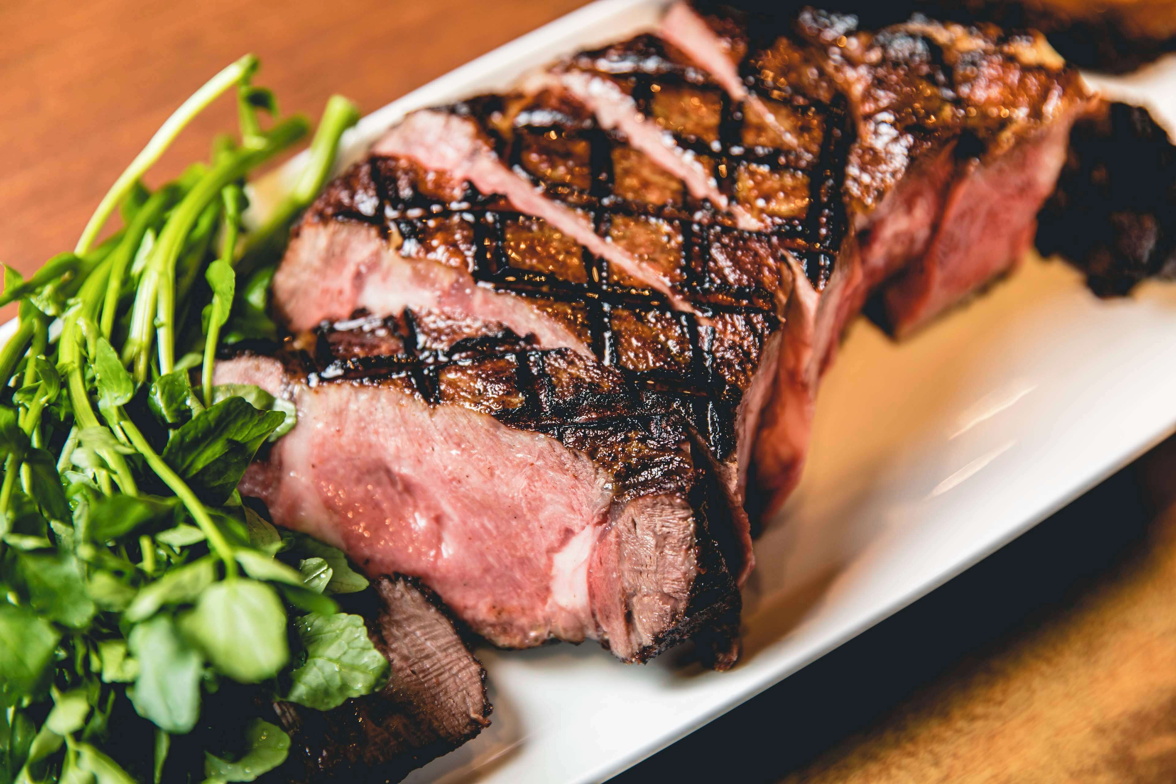 Een gegrilde steak met braadstrepen op een wit bord, vergezeld van een groene salade.