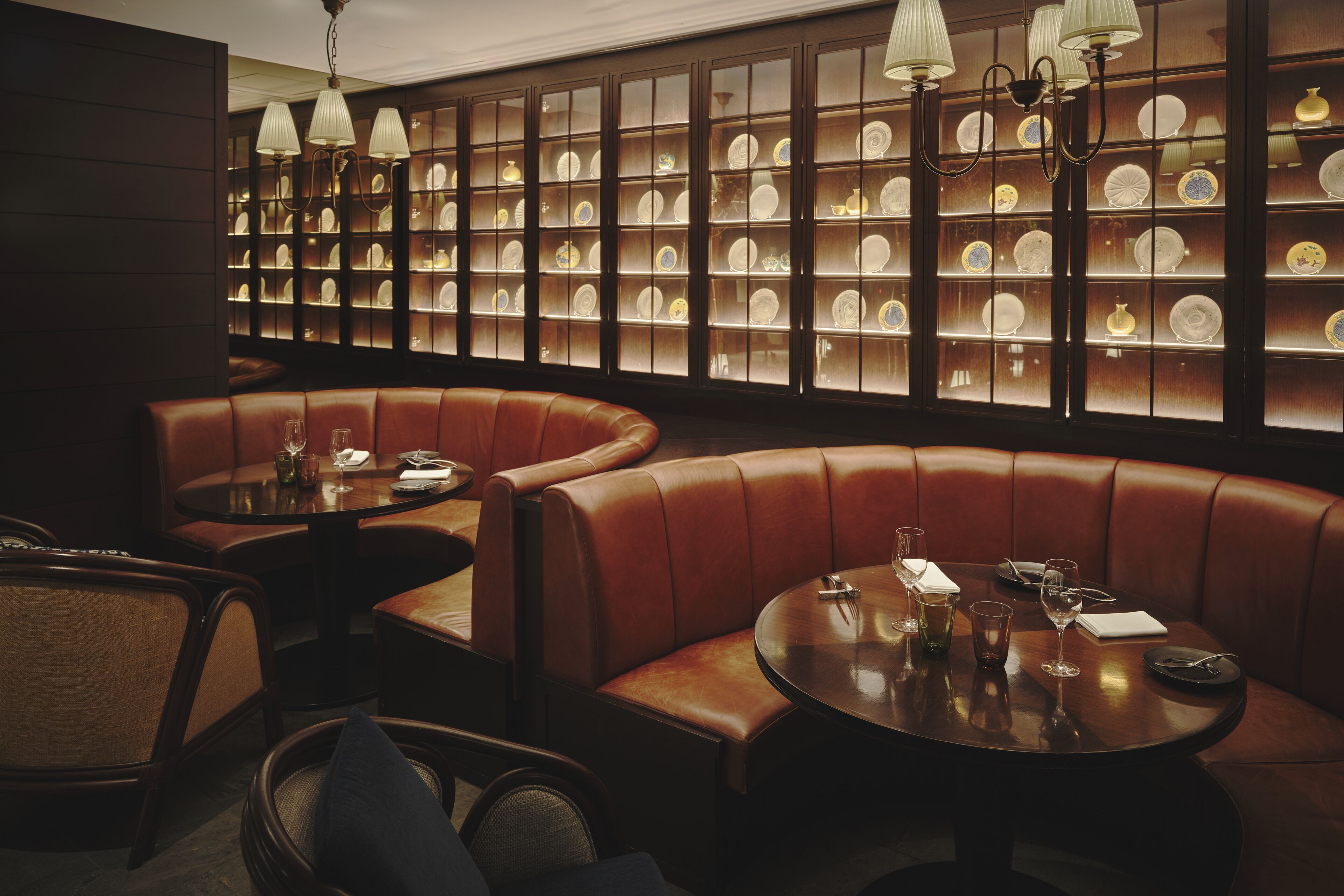 A restaurant with leather booths, round tables, and a wall of glass display cases.