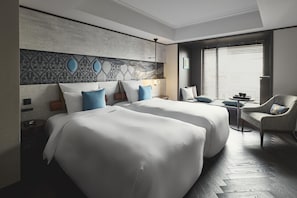 Habitación de hotel con dos camas, un sofá, una mesita y vistas al exterior.