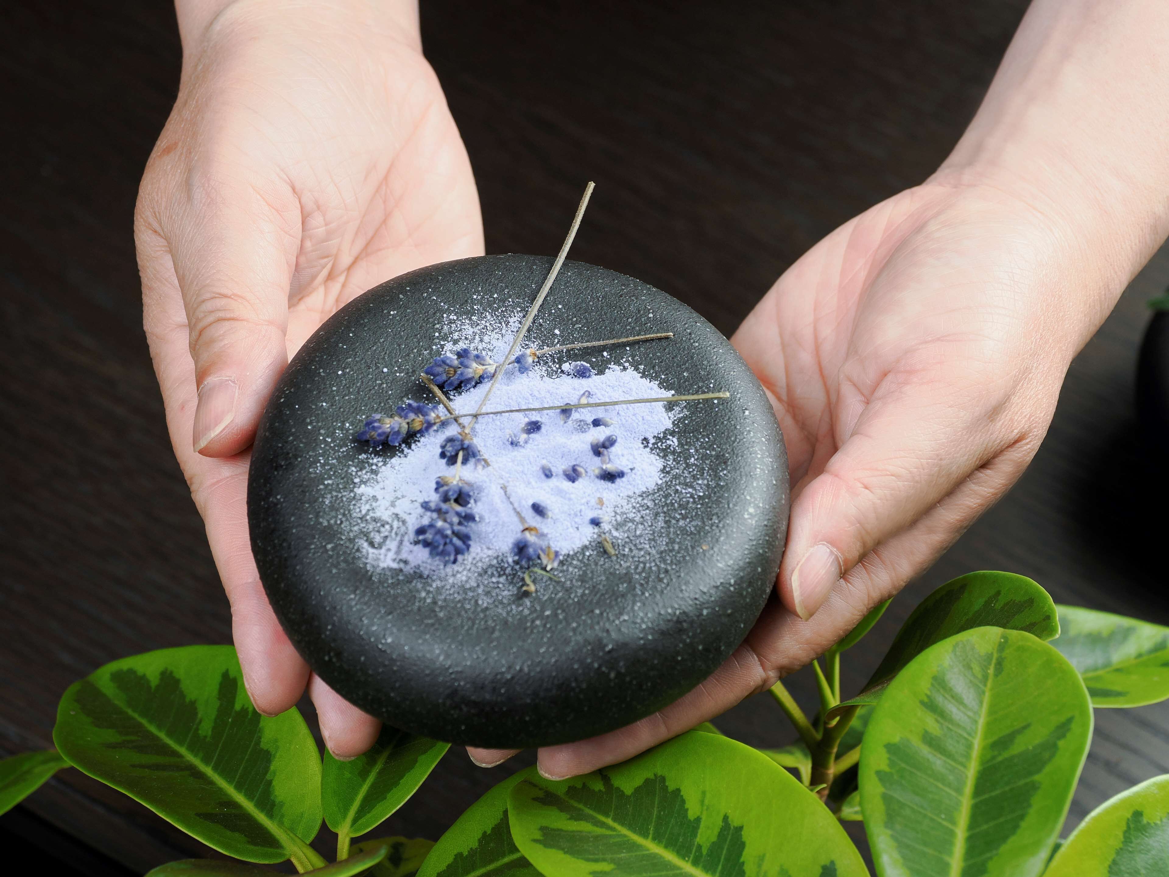 A person holding a black stone with blue flowers and a stick.
