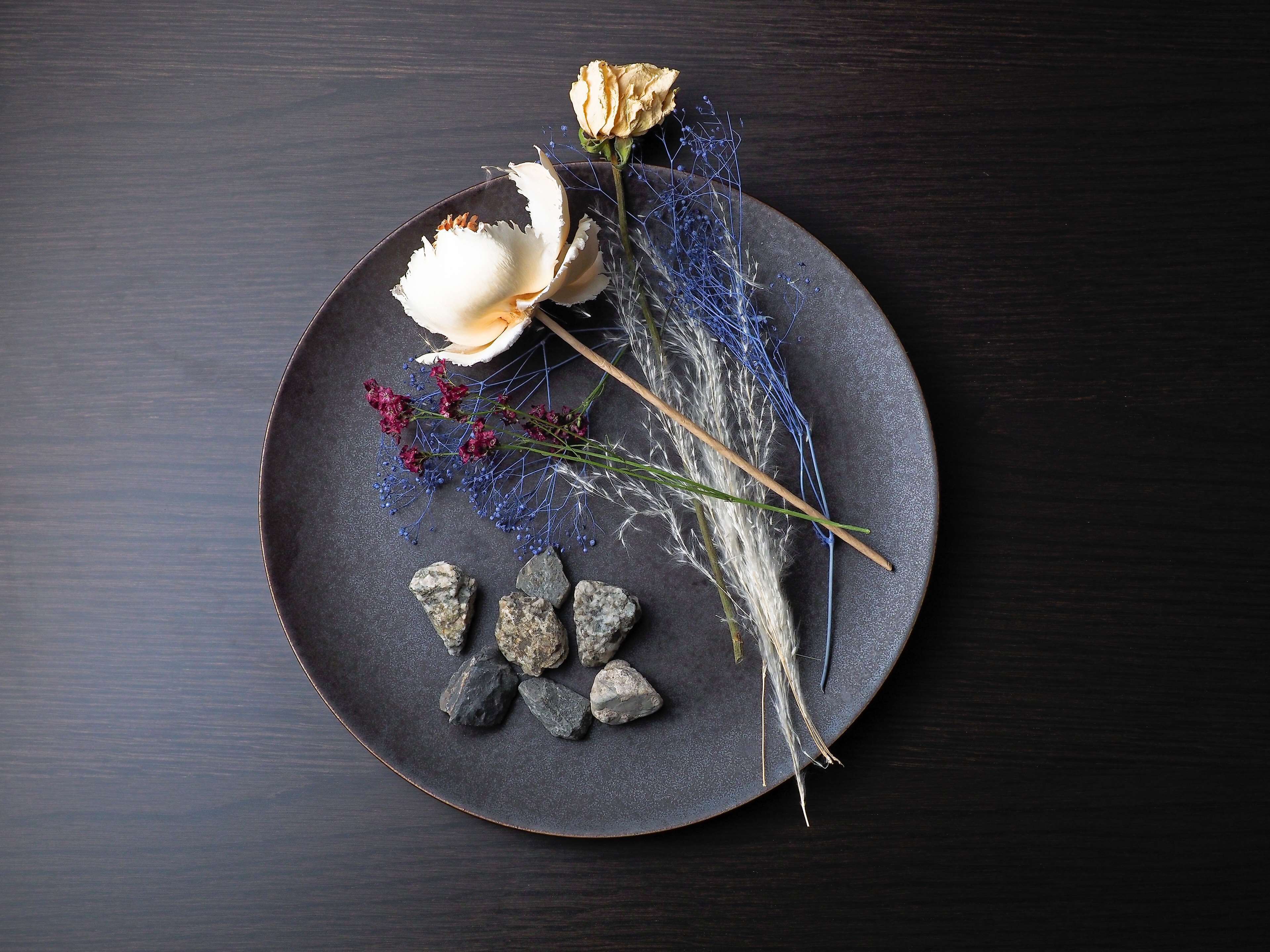 A dark plate with a white flower, dried flowers, and rocks.