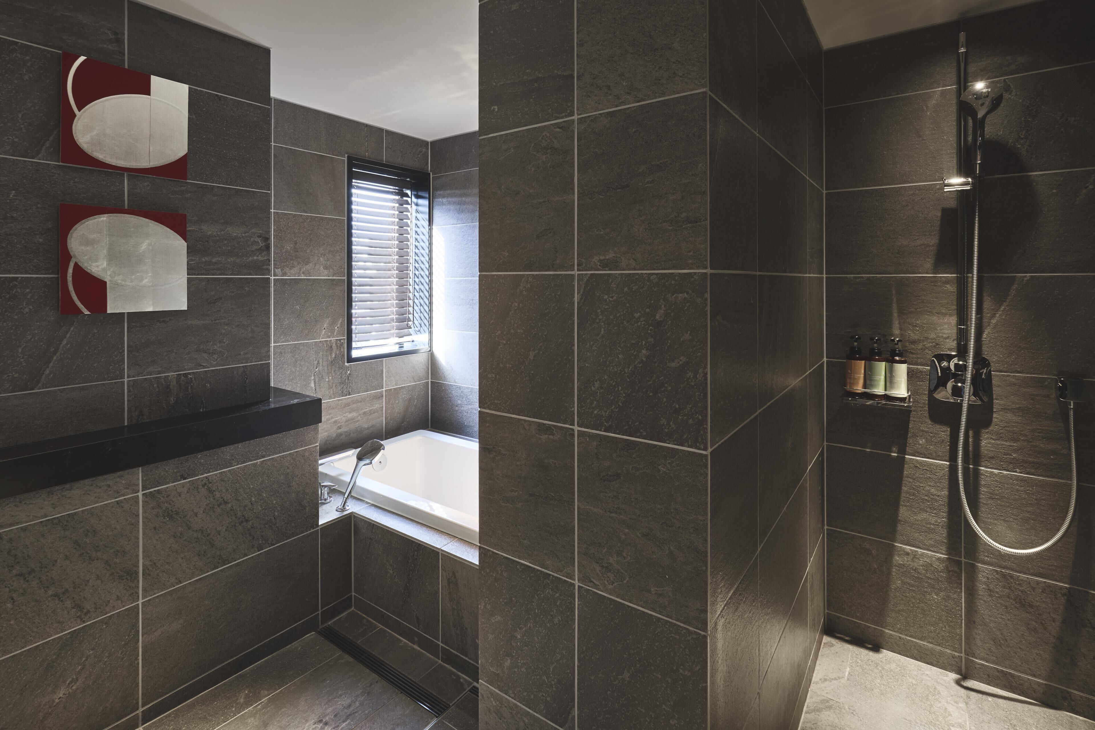 A modern bathroom with dark tiles, a bathtub, a shower, and two wall-mounted mirrors.