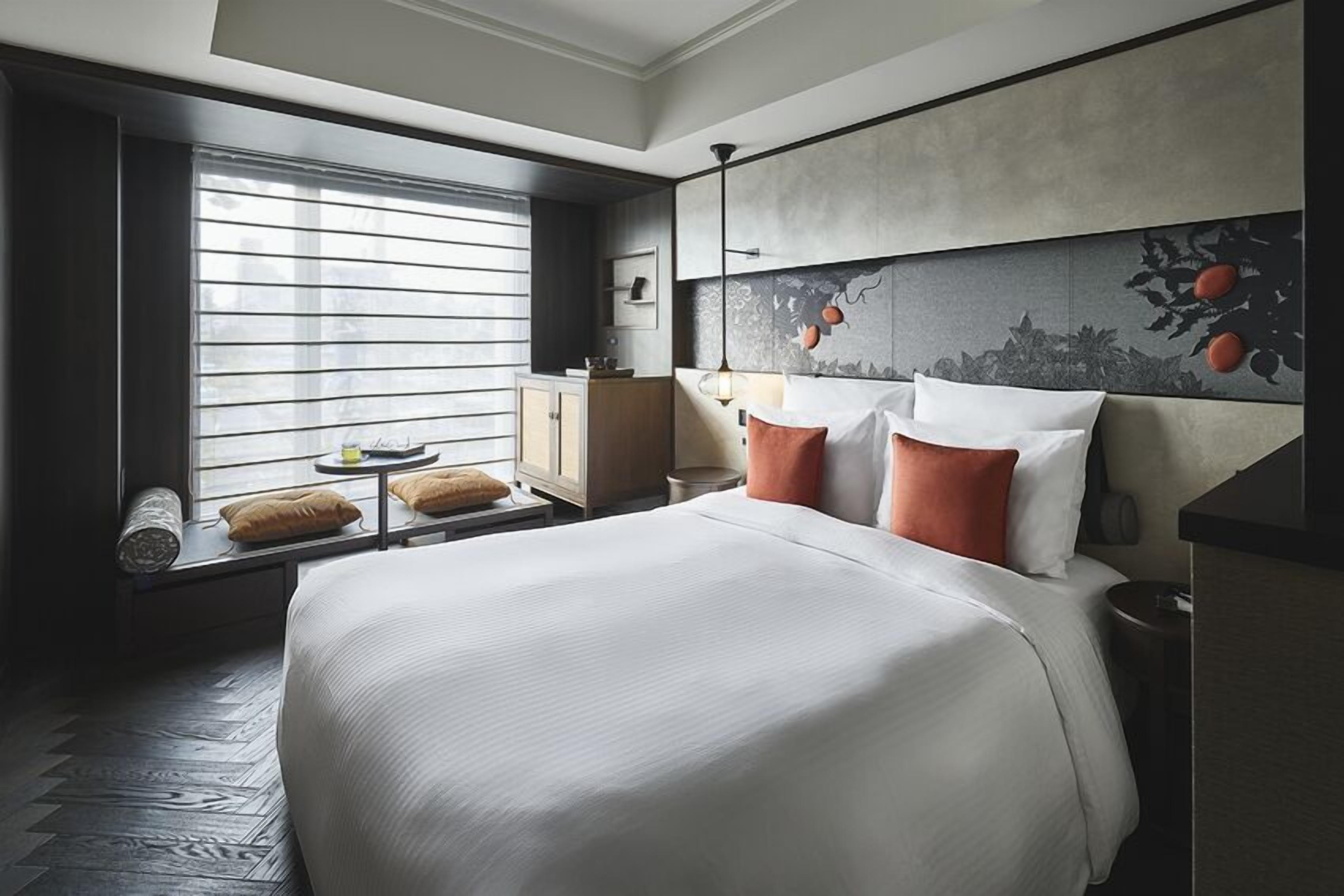 Een hotelkamer met een groot bed, een raam met zonwering, een nachtkastje en een wandplank.