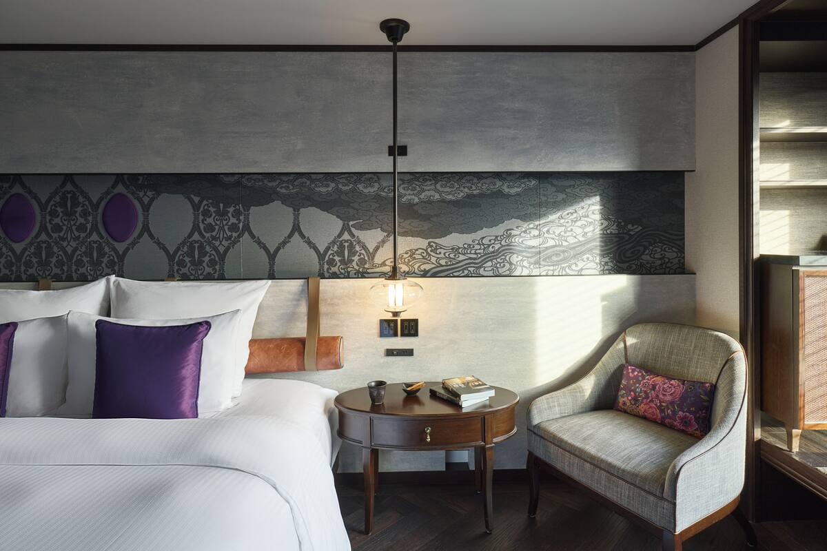 Une chambre d’hôtel comprenant un lit, une petite table ronde, une chaise, une lampe et un mur décoratif.