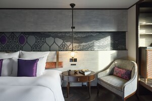 Quarto de hotel com cama, mesa auxiliar redonda, uma cadeira, abajur e decoração na parede.