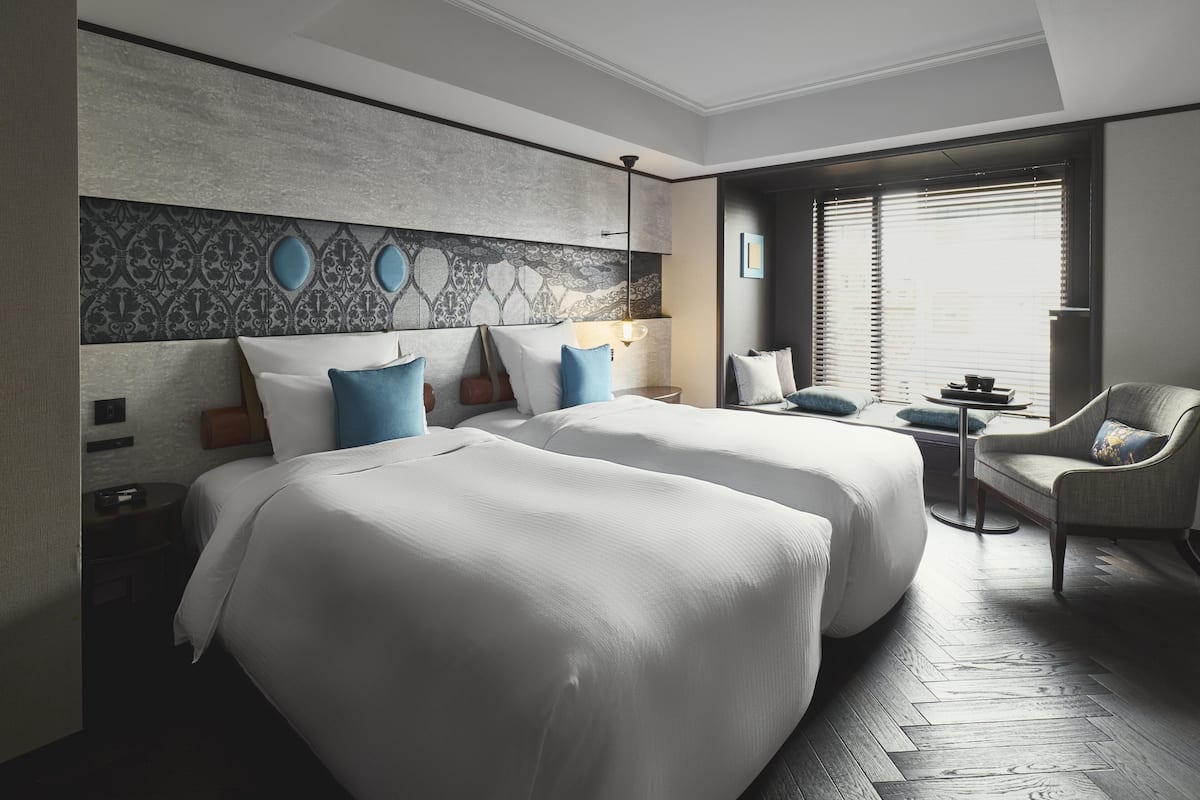 Ein Hotelzimmer mit zwei Betten, einem Schlafsofa, einem kleinen Tisch und Blick ins Freie.