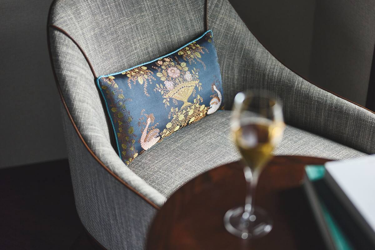 Une chaise avec un coussin à motifs et un verre de vin blanc sur une table.
