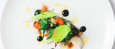 A white plate with a dish of food, including greens, tomatoes, and olives.