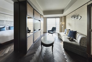 Une chambre d’hôtel moderne, équipée d’un lit, d’un canapé, d’une table basse ronde et d’une grande fenêtre avec des stores.