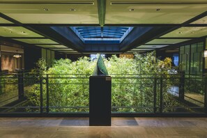 Un intérieur moderne avec un garde-corps central en verre, une verrière et une vue sur la verdure intérieure.