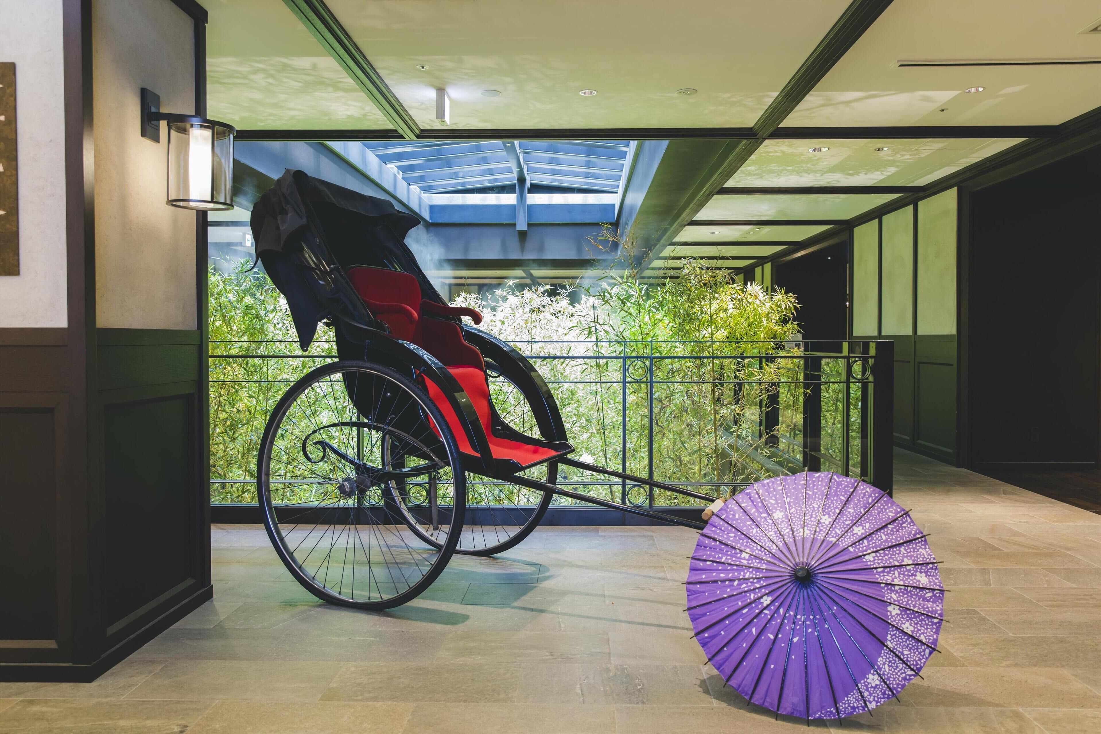 A wheelchair, a purple umbrella, and a view of greenery through a glass wall.