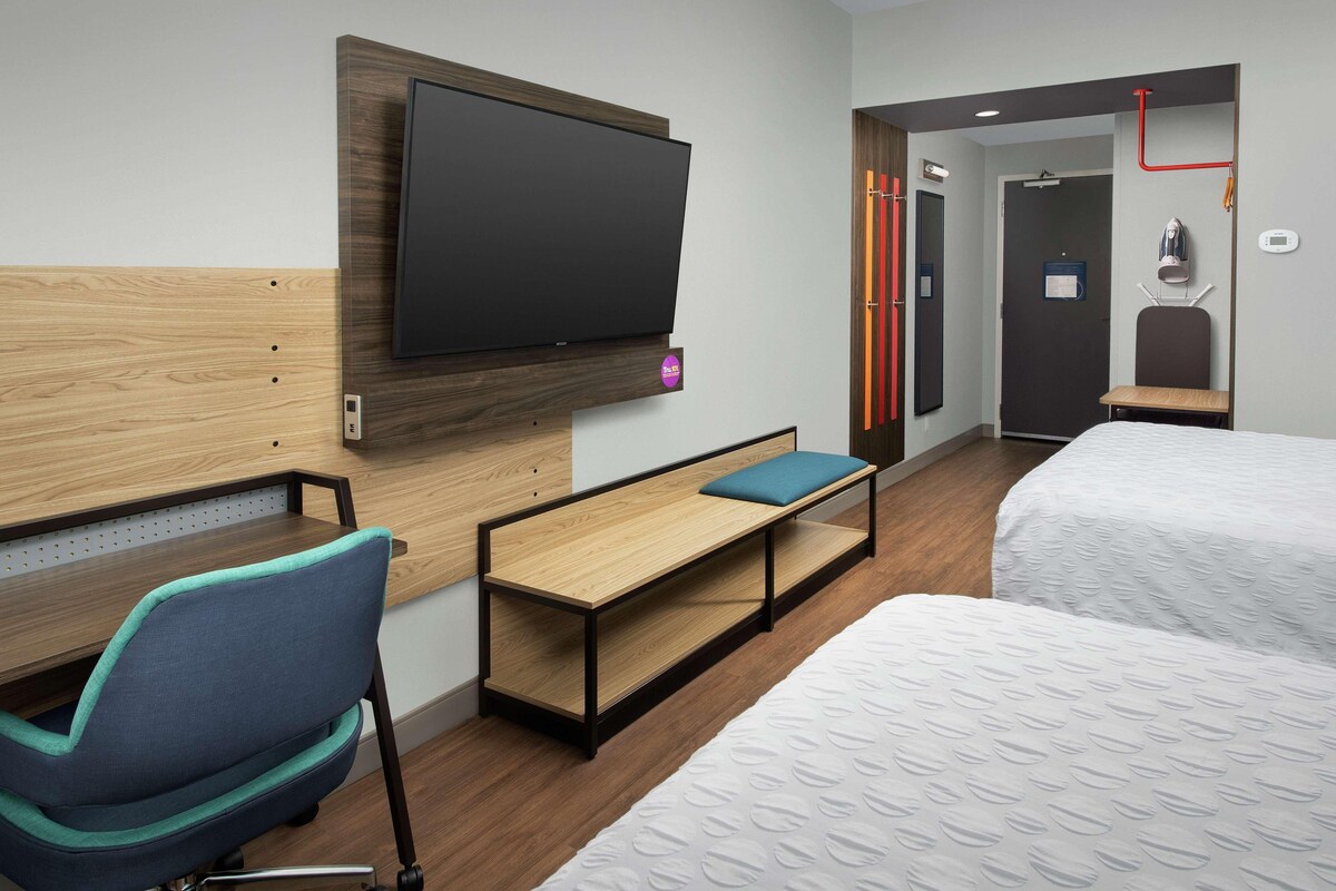 A hotel room with a bed, a desk, a chair, a TV, and a shower area.