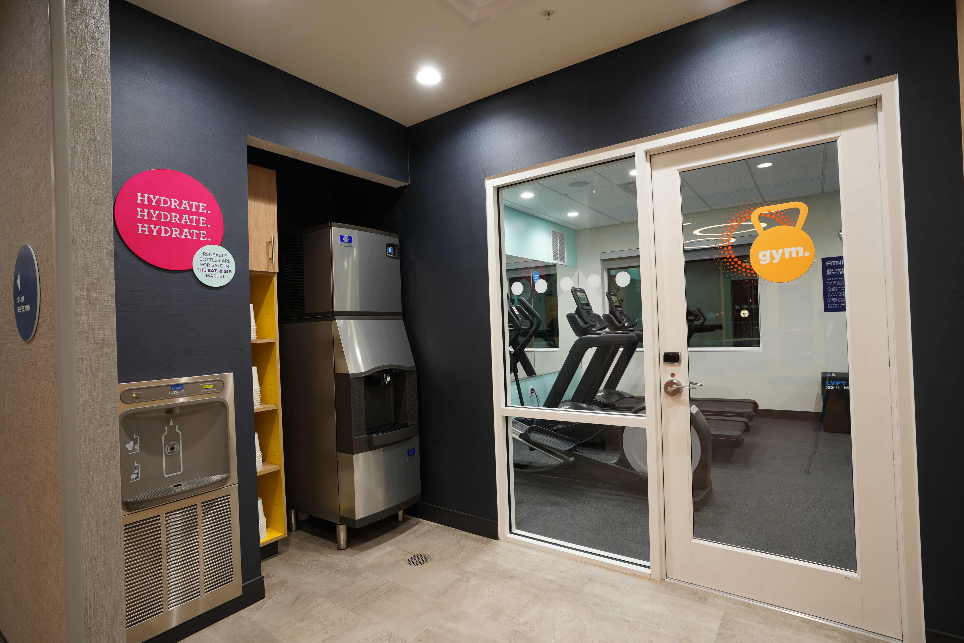 A gym area with a water dispenser, a treadmill, and a mirrored wall.