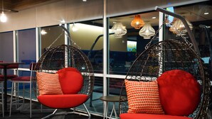 A modern interior with two red chairs and a small table, large windows, and hanging pendant lights. - Tru by Hilton Lake City (Lake City)
