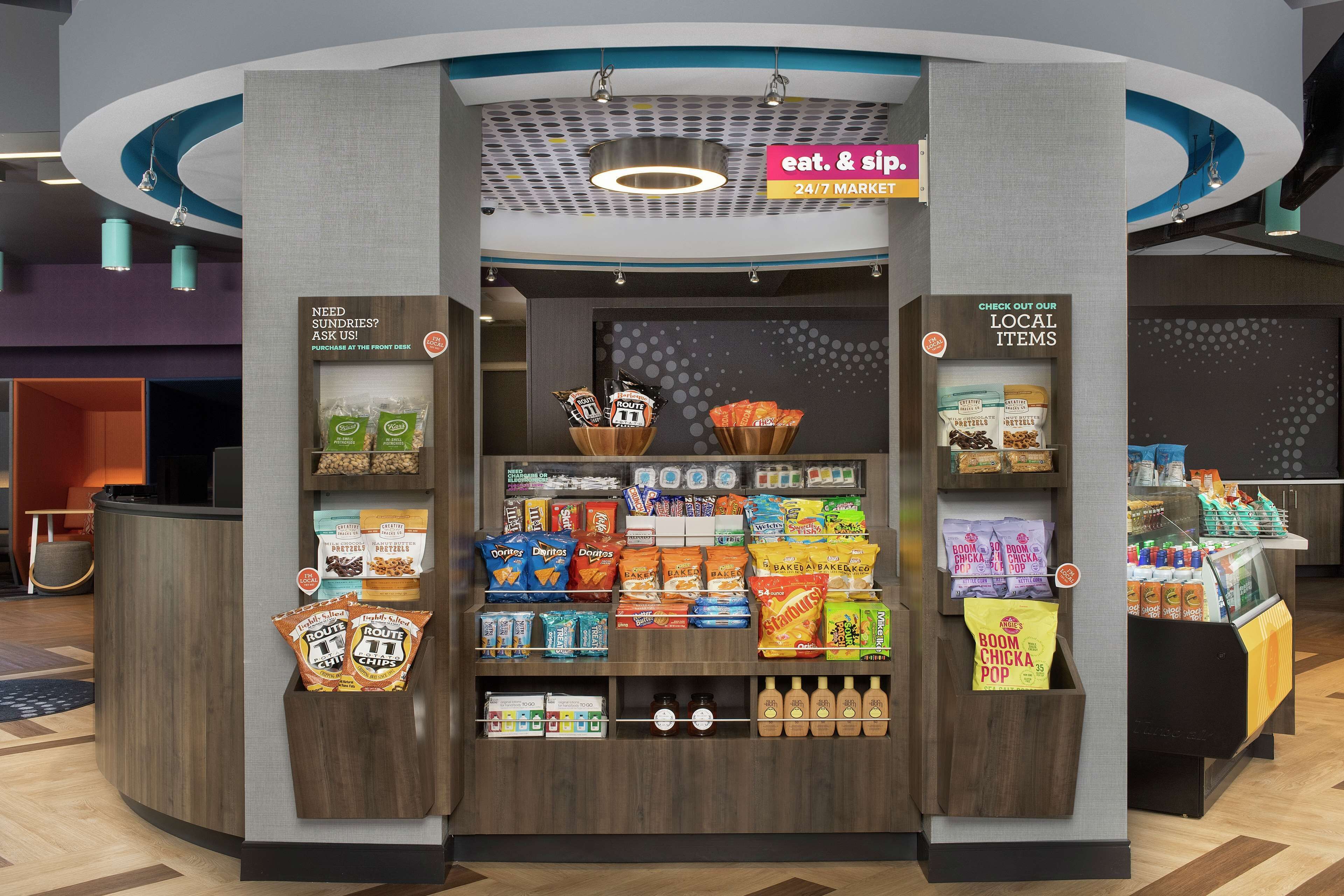 A snack kiosk with a variety of packaged snacks and beverages, a sign indicating a 24/7 market, and a counter for customer service.