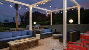 An outdoor patio with a stone fire feature, blue cushioned seating, and a grill. - Tru by Hilton Lake City (Lake City)