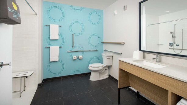 A modern bathroom with a white toilet, a sink with a mirror, and a blue wall with circular patterns. - Tru by Hilton Lake City (Lake City)