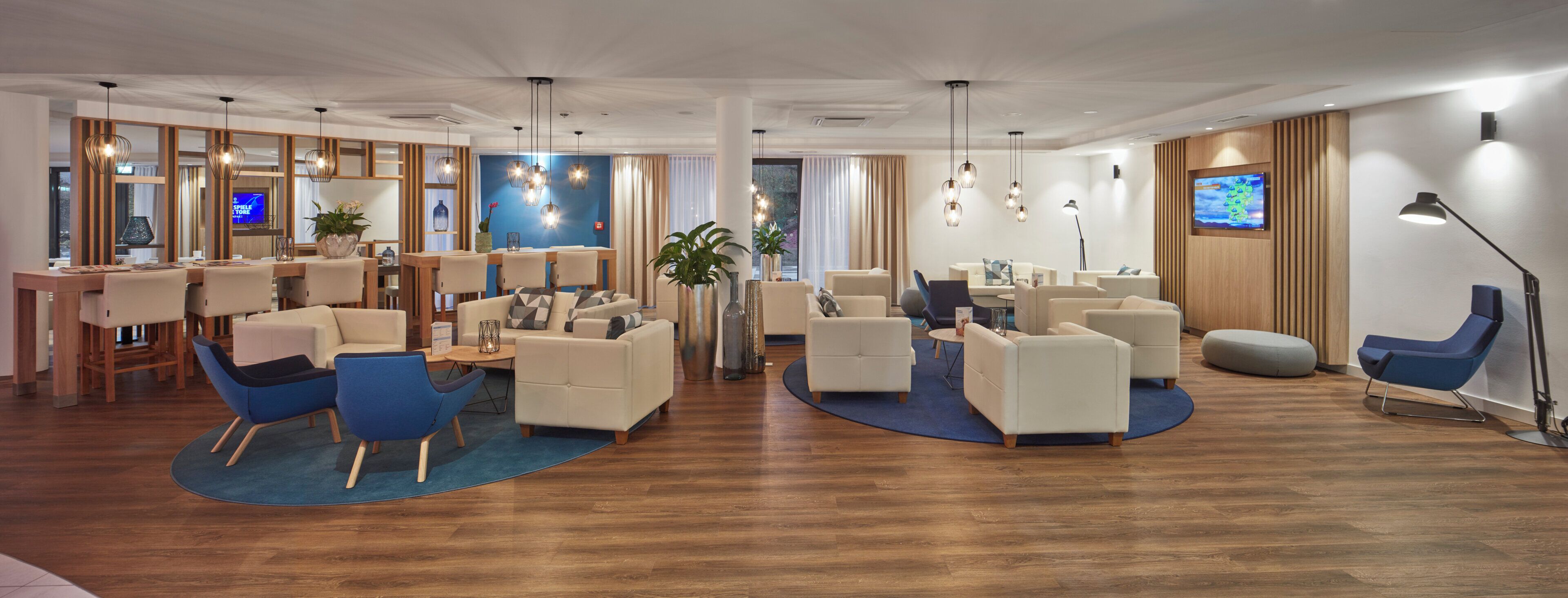 A hotel lobby with a reception desk, seating area, and a TV screen.