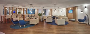 A hotel lobby with a reception desk, seating area, and a TV screen.