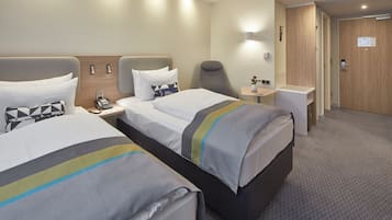 Una habitación de hotel con dos camas, un escritorio, una silla y una mesita con un florero.