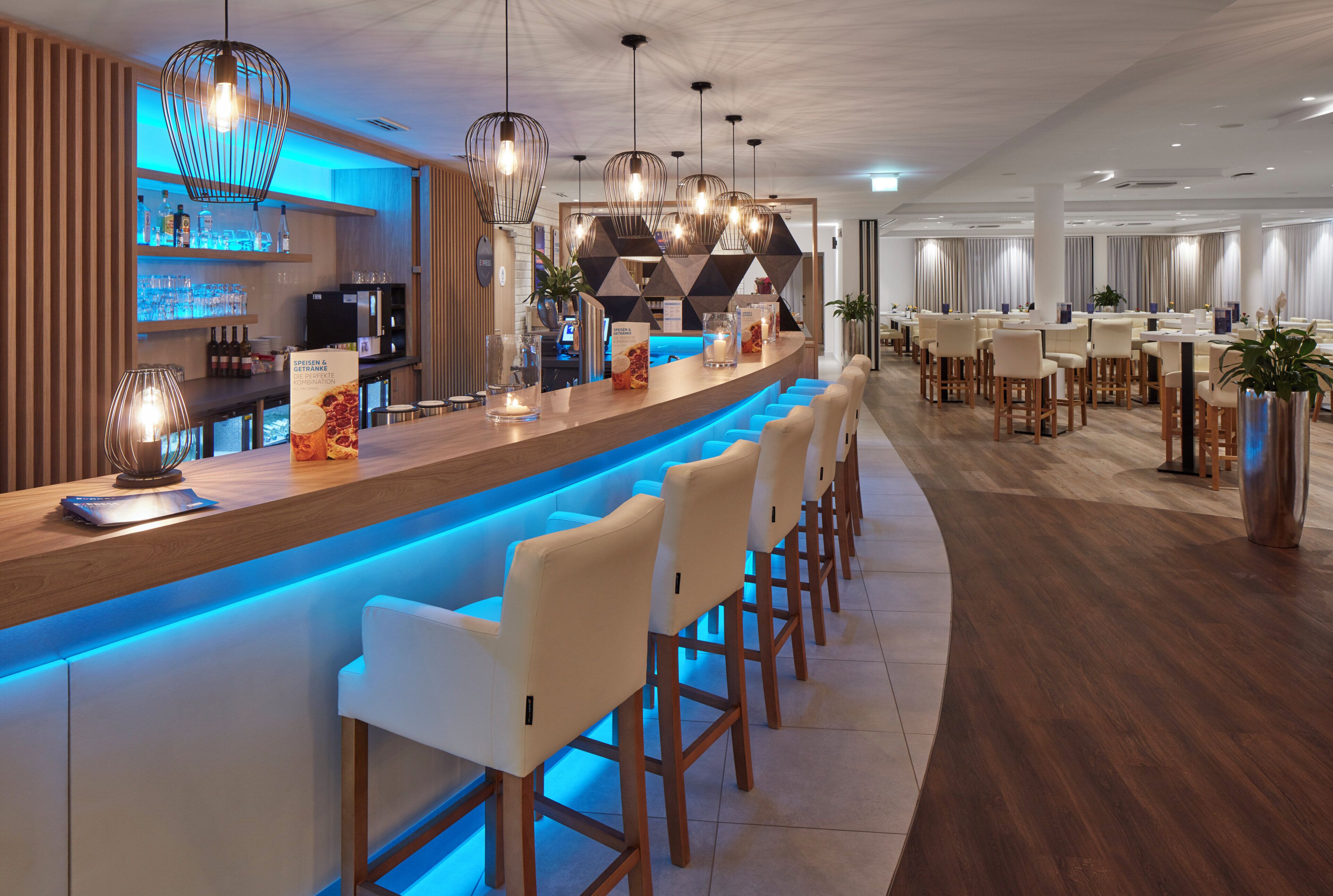 A modern bar area with a long counter, bar stools, and pendant lighting.