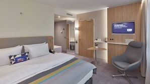 Una habitación de hotel con cama, escritorio, silla, televisor y una mesita.