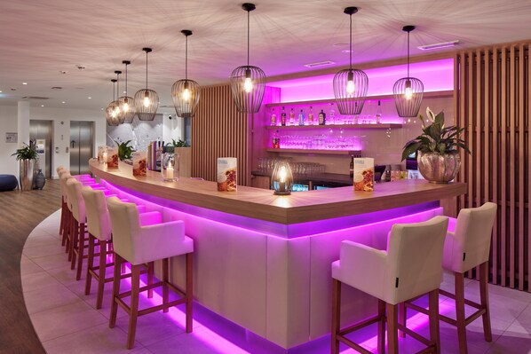 Zona de bar moderna con una isla central, taburetes, iluminación colgante y una barra repleta de botellas.