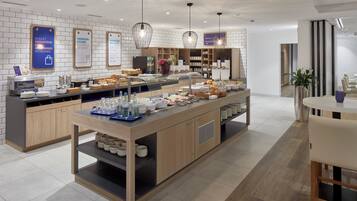 En modern frukostbuffé med ett varierat utbud av mat, en kaffestation och en sittplats med bord och stolar.