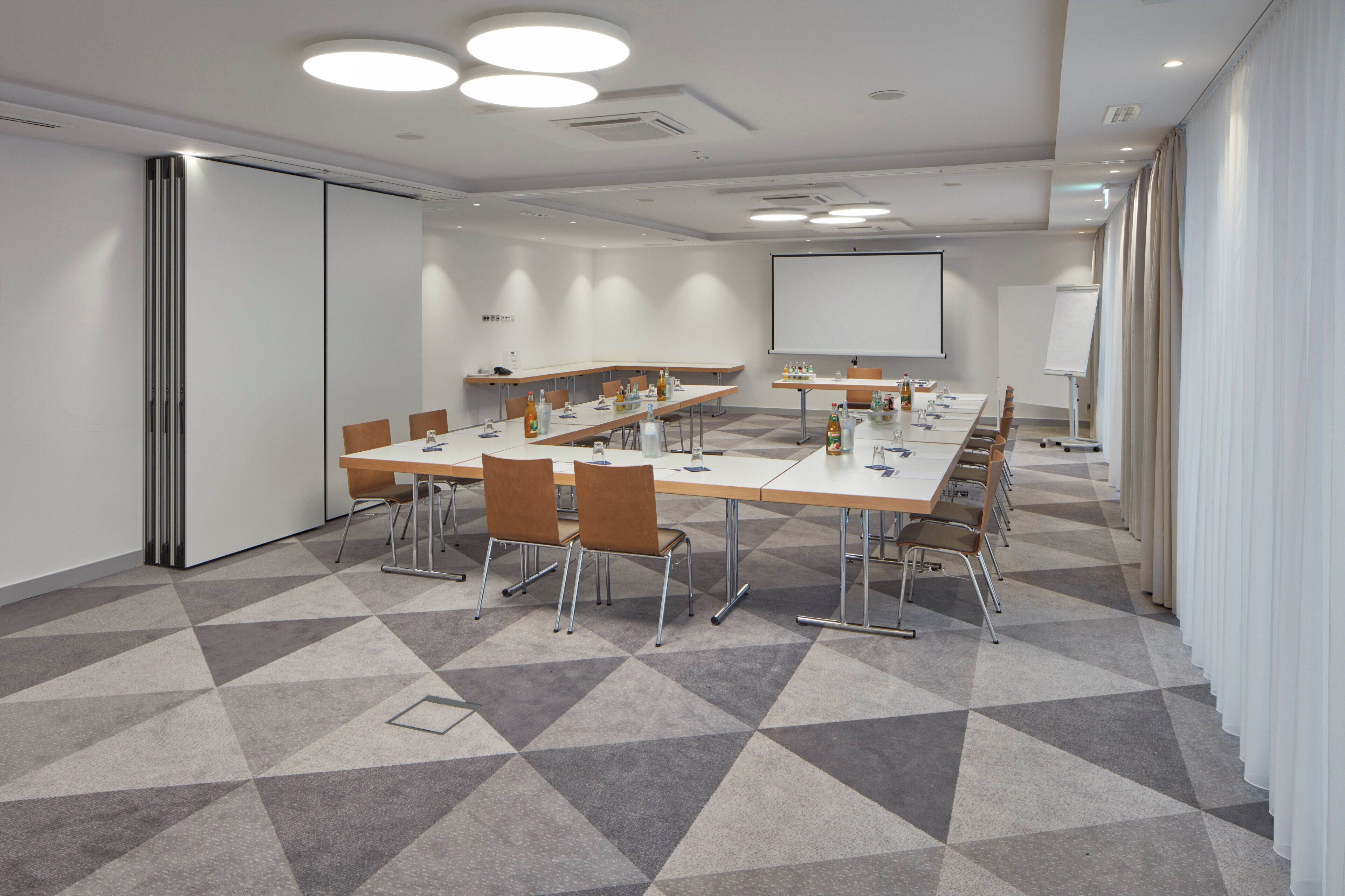 Ein Konferenzraum mit einem langen Tisch, Stühlen, einer Projektionsleinwand und einer Whiteboard-Tafel.