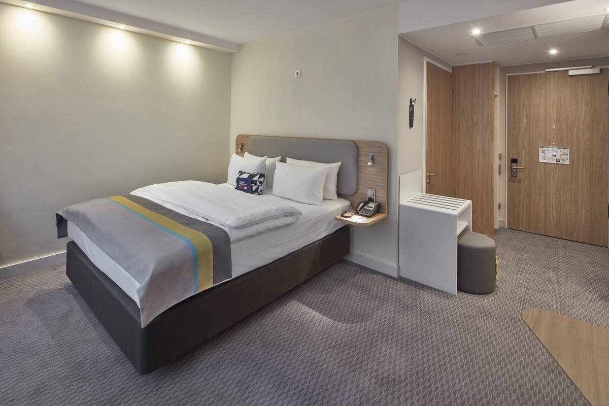 Et moderne hotelværelse med en stor seng, et sengebord og et lille skrivebord.
