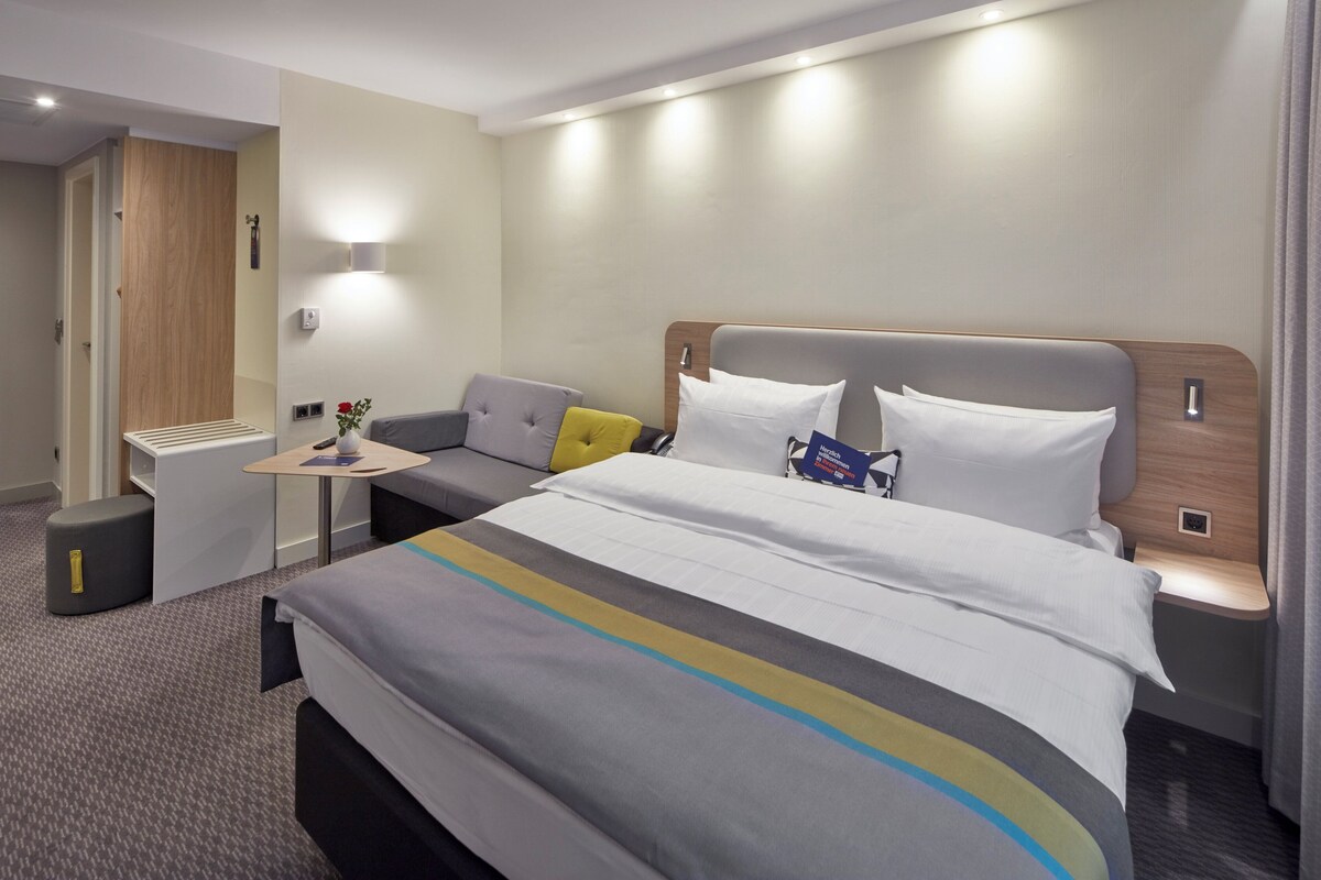 A hotel room with a bed, a small table, a sofa, and a nightstand.