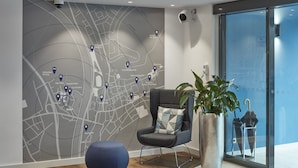 Un moderno vestíbulo de hotel con un mapa grande en la pared, un espacio de descanso acogedor y una planta en maceta de gran tamaño.