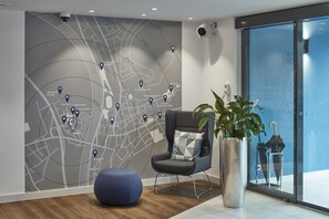 Een moderne hotellobby met een grote kaart aan de muur, een comfortabele zithoek en een grote potplant.