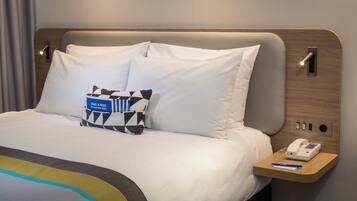 A neatly made bed with white linens, a bedside table with a phone and pen, and a pillow with a blue tag.