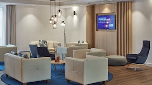 Un moderno vestíbulo de hotel con zona de estar que incluye sofás y sillones, una mesa de centro redonda y un televisor de pantalla plana montado en la pared.