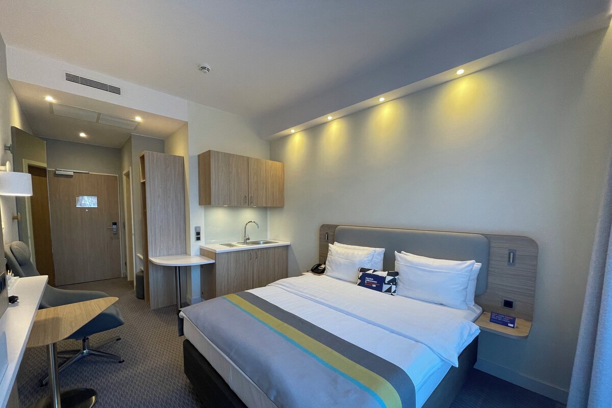 A hotel room with a bed, desk, and kitchenette.