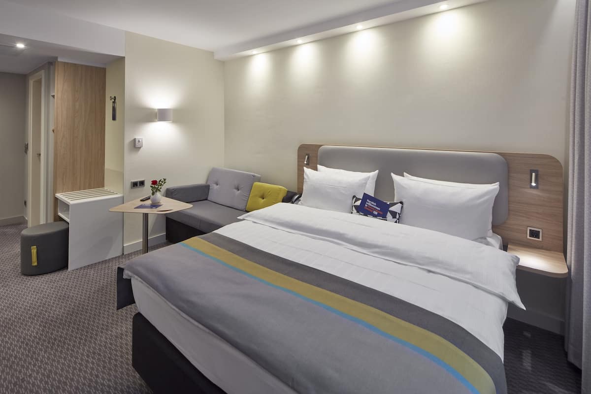 Et moderne hotelværelse med en stor seng, et lille skrivebord og en sofa.