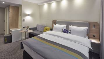 Ein modernes Hotelzimmer mit einem großen Bett, einem kleinen Schreibtisch und einem Schlafsofa.