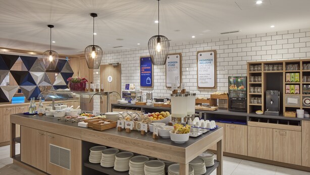 Una barra de desayuno moderna con una variedad de alimentos y bebidas, armarios de madera y un salpicadero de azulejos.