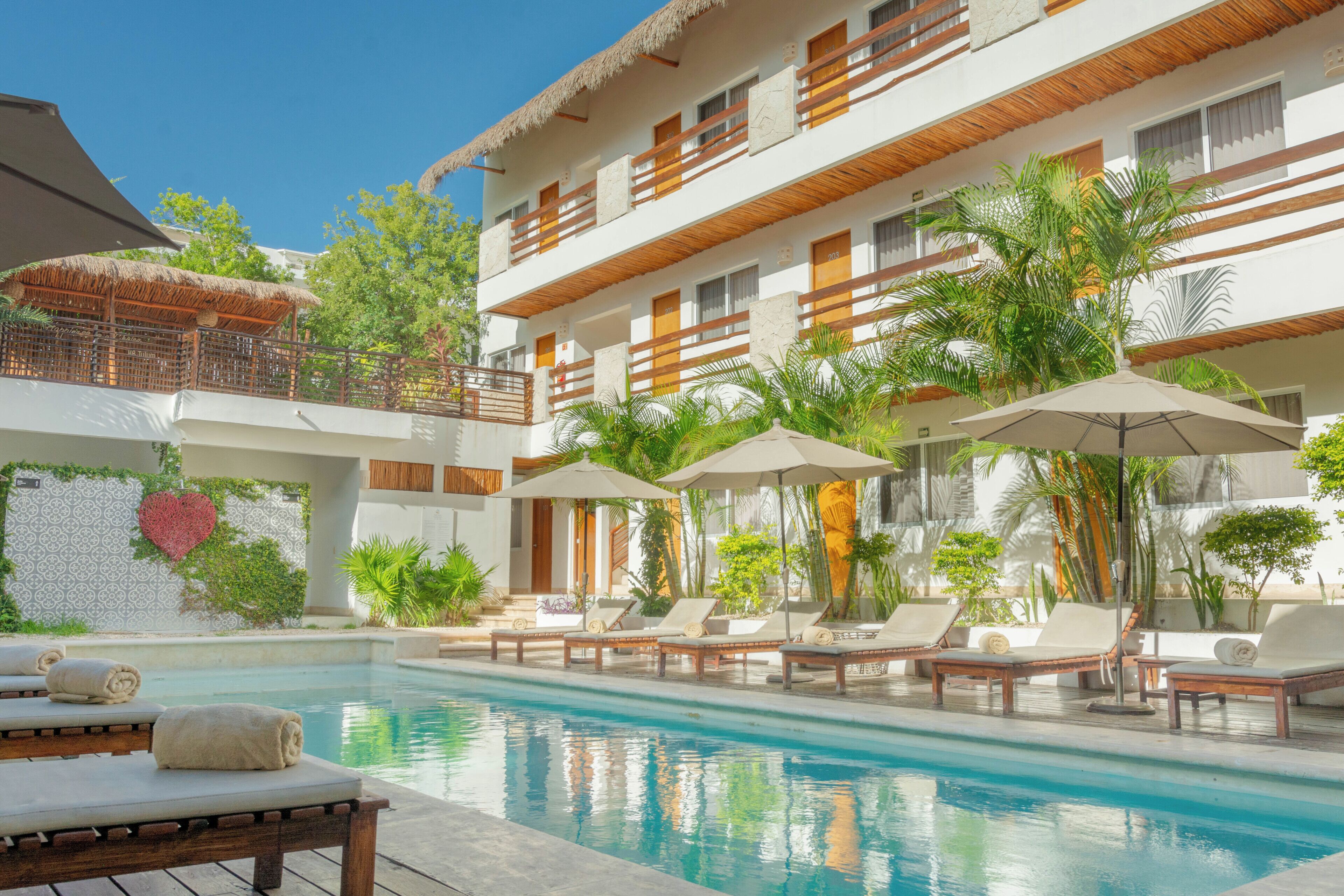 A hotel with a pool, lounge chairs, umbrellas, and a heart-shaped decoration.