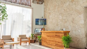 Un área de recepción con un mostrador de madera, una pared de piedra y un ventanal con cortinas translúcidas.
