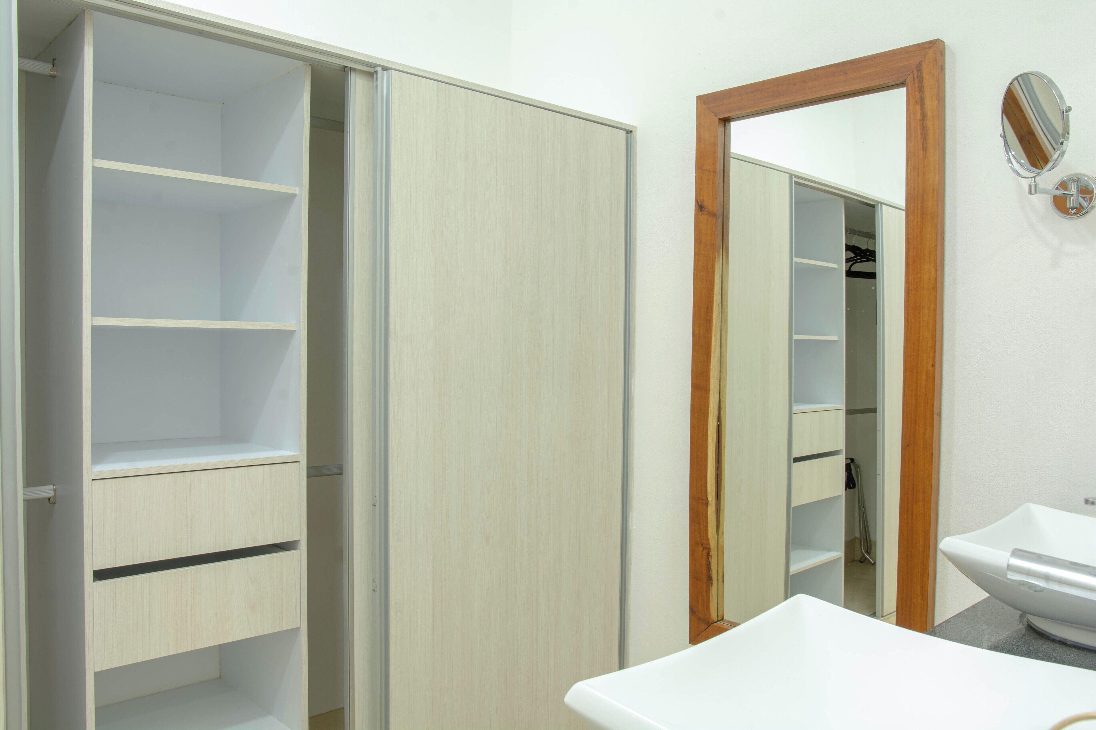 Un bagno con un lavandino bianco, uno specchio e un armadio con diversi ripiani.