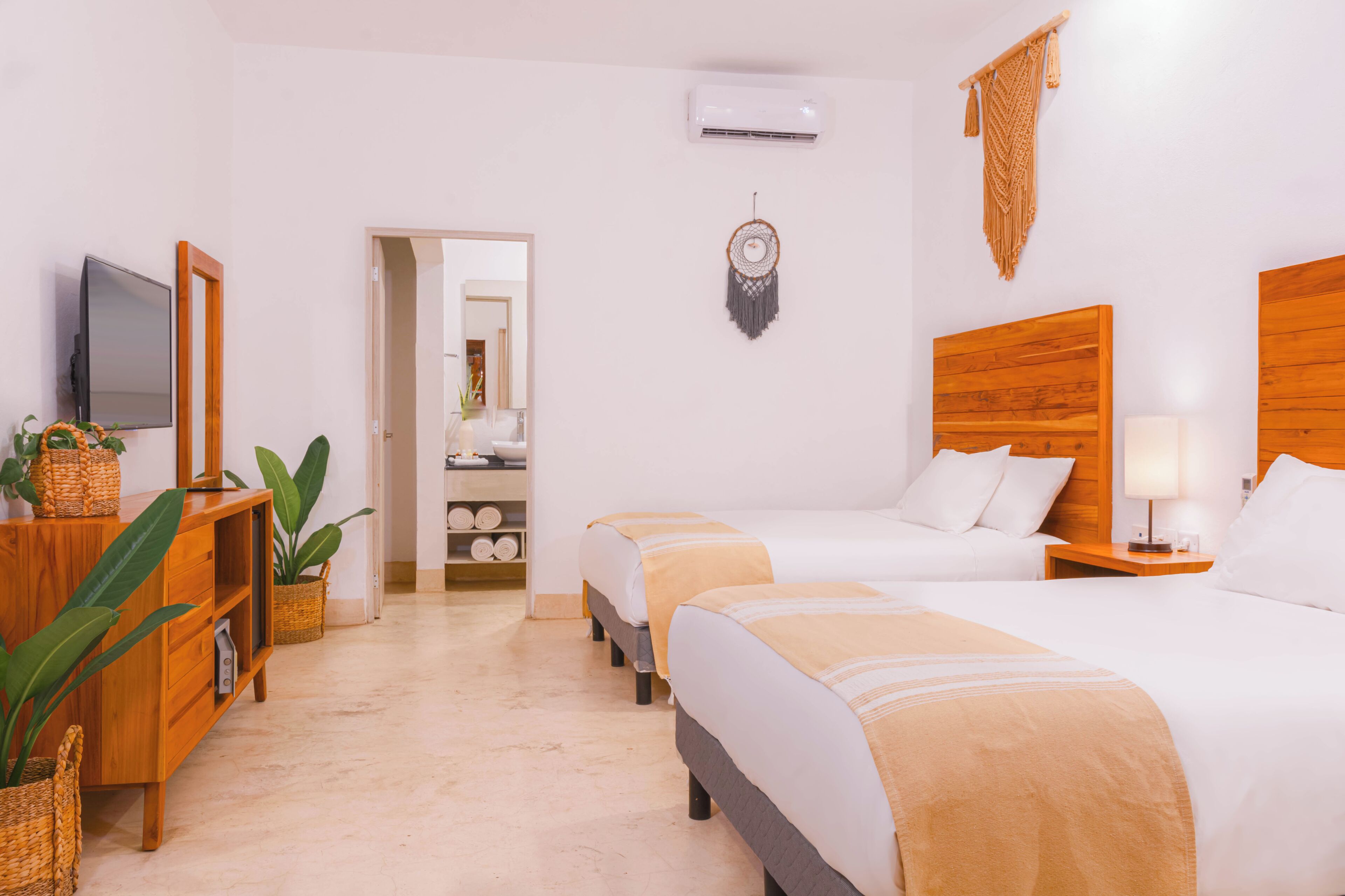 A hotel room with two beds, a TV, a wardrobe, a bedside table with a lamp, and a dreamcatcher on the wall.