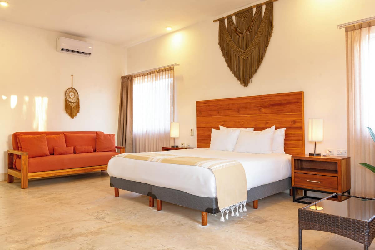 Una habitación de hotel con cama, sofá, mesita de noche, lámpara y un cuadro en la pared.