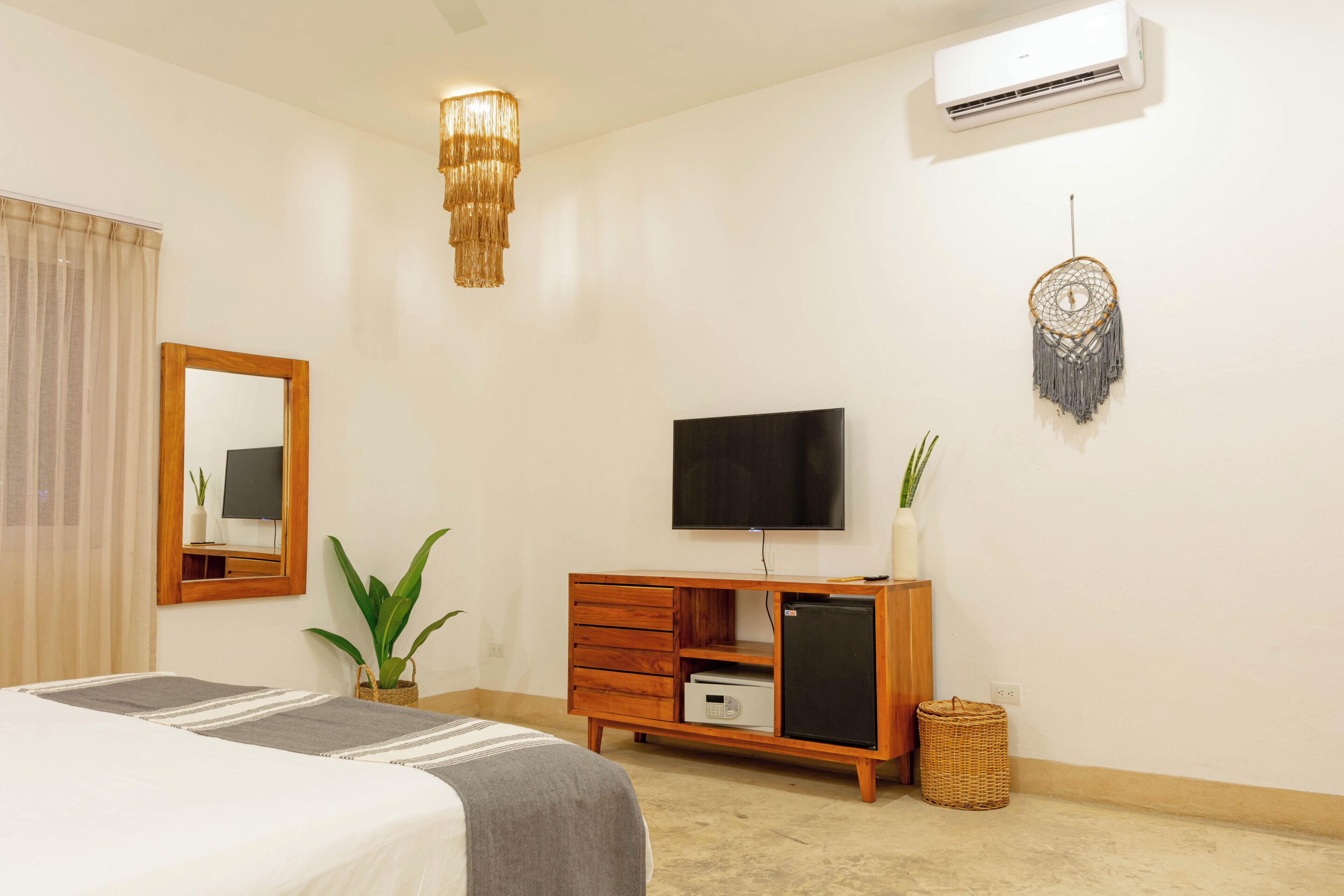 Een slaapkamer met een bed, een houten dressoir, een televisie, een droomvanger en een luchtverfrisser aan de muur.