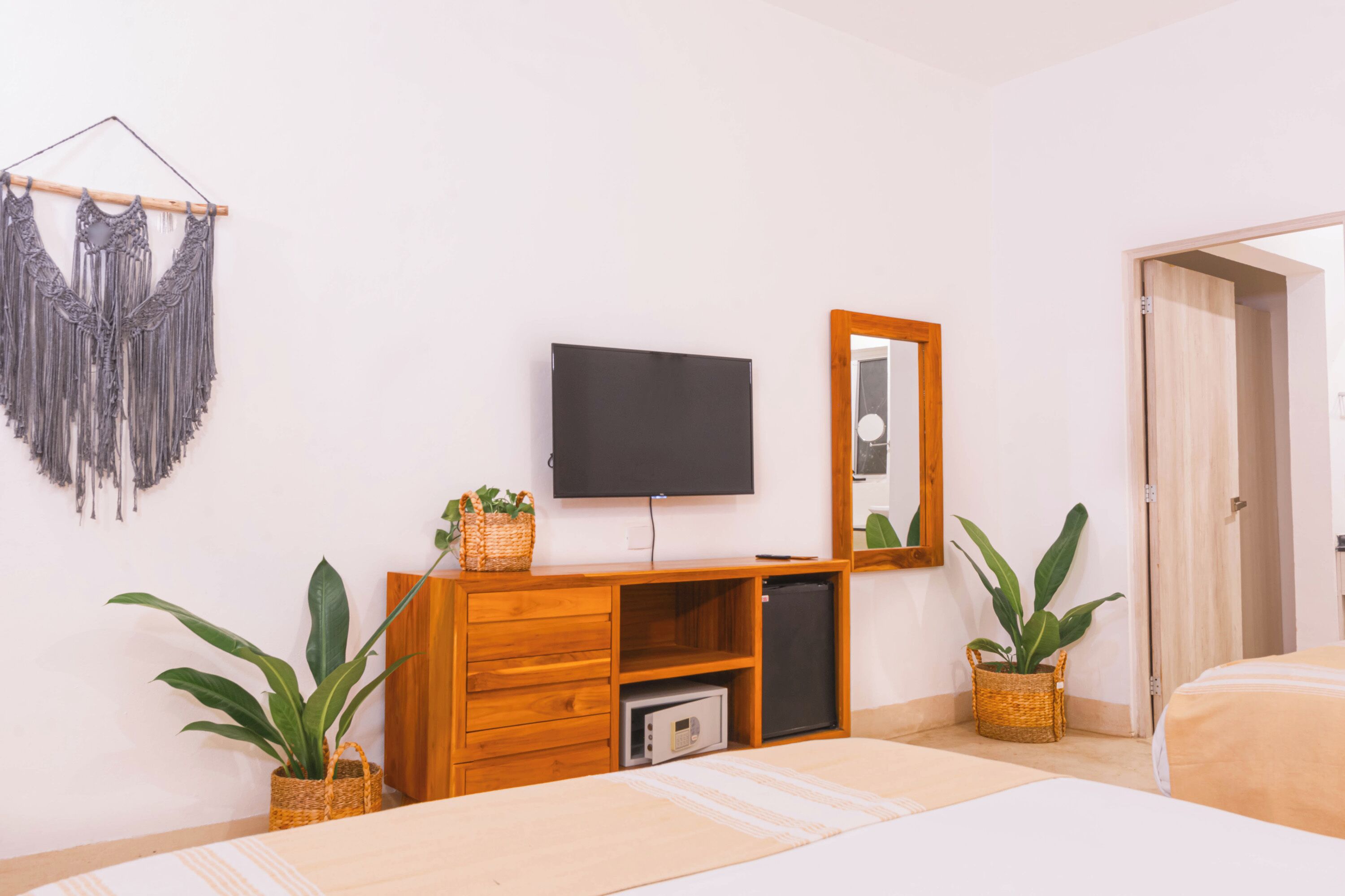 Un dormitorio con cama, cómoda de madera, televisor, espejo y plantas en macetas.
