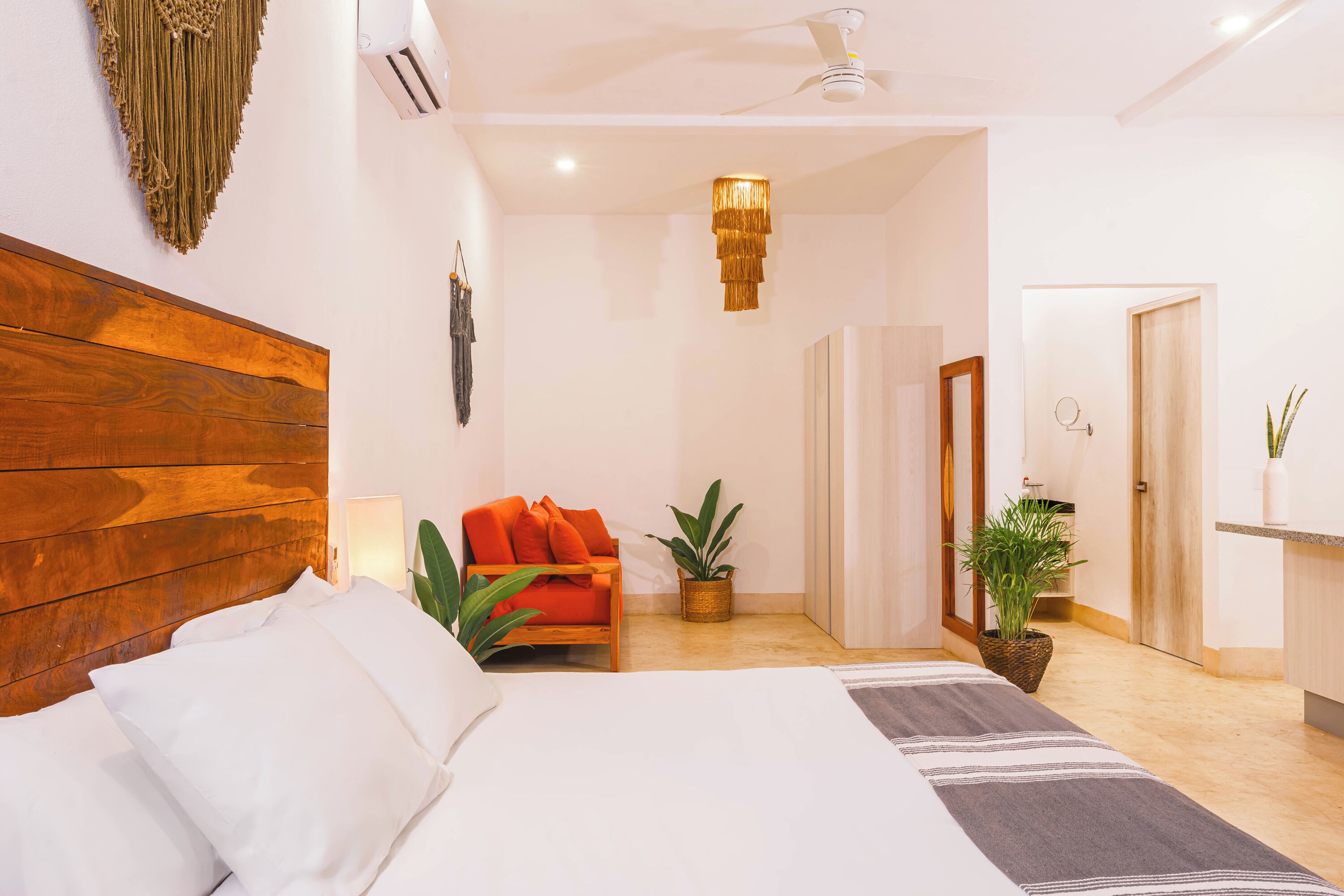 Un dormitorio con cabecera de madera, cama con ropa de cama blanca, un sofá rojo y una pequeña mesa con una planta.