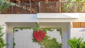 Fachada de edificio con pared decorativa, diseño en forma de corazón y vegetación.